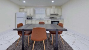 Une cuisine compacte avec des meubles blancs, un réfrigérateur, un four à micro-ondes, une cuisinière et une table à manger avec quatre chaises.