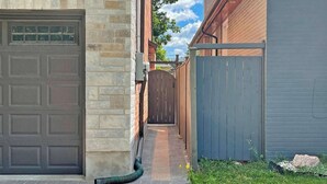 Une allée étroite mène à un garage dont un côté est bordé d’un mur de briques et l’autre d’une clôture en bois.