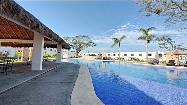 A swimming pool with lounge chairs and a thatched-roof structure.