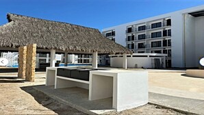 A modern building with a pool area, including a thatched-roof structure and a white poolside bar.