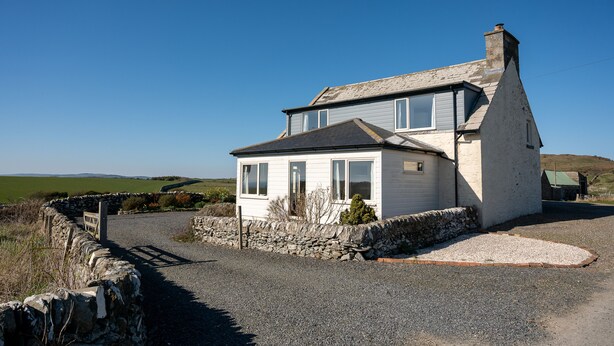 A white house with a stone wall driveway, a chimney, and a view of the countryside.