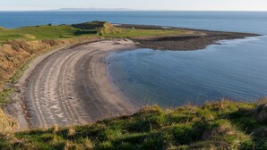 A coastal road curving along a beach with a golf course in the background.