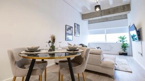 Una sala moderna con una mesa de comedor de vidrio, dos sillones, un sofá y un ventanal que proporciona luz natural.
