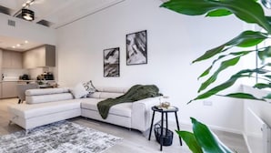 Un salón moderno con un sofá seccional blanco, una mesita auxiliar y dos cuadros abstractos en la pared.