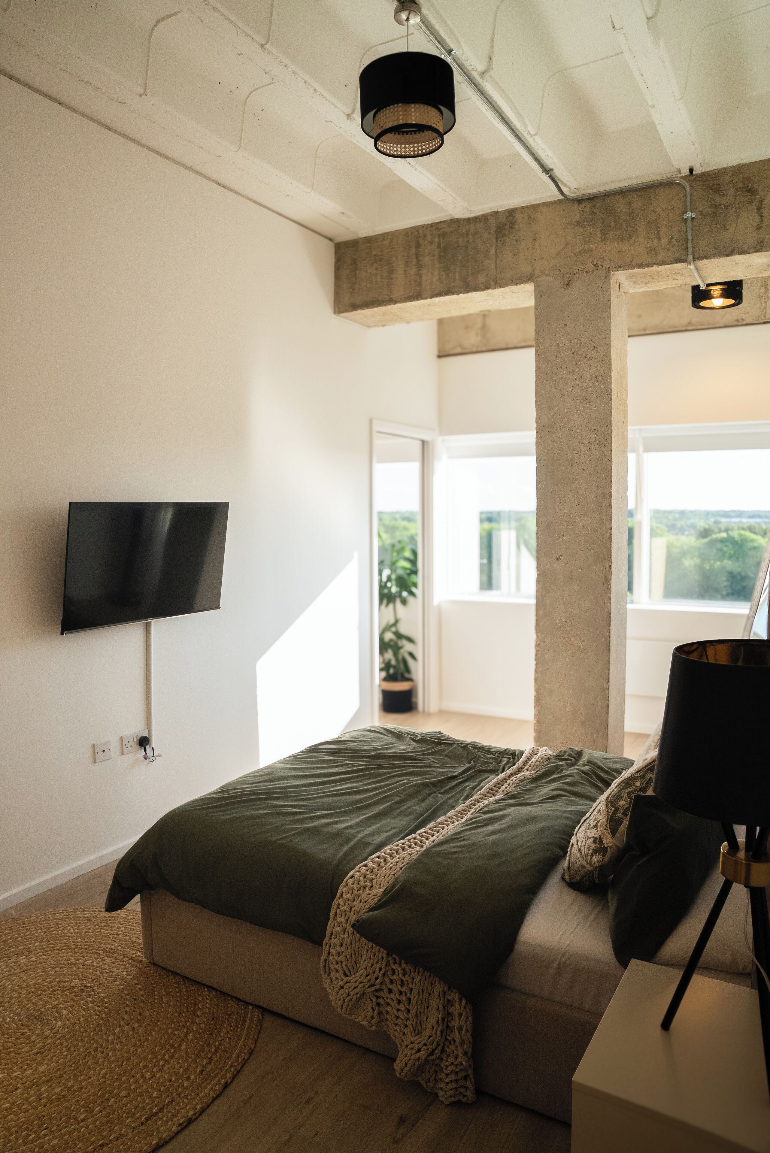 Une chambre moderne avec un grand lit, un téléviseur fixé au mur et un balcon avec vue.