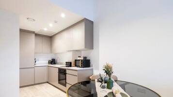 A modern kitchen with built-in appliances, a dining table with a glass top, and a small seating area.
