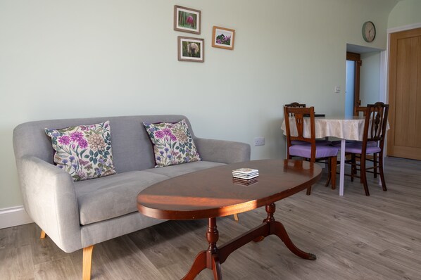 Una sala de estar con un sofá gris, una mesa de centro de madera y una mesa de comedor con sillas.