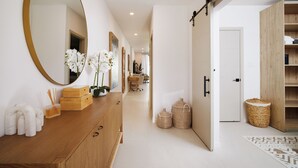 A modern hotel hallway with a wooden vanity, a large mirror, white orchids, and a woven basket.