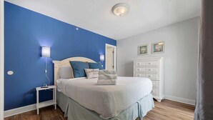 Une chambre à coucher comprenant un lit, une table de chevet, une commode, un meuble à tiroirs et une lampe fixée au mur.