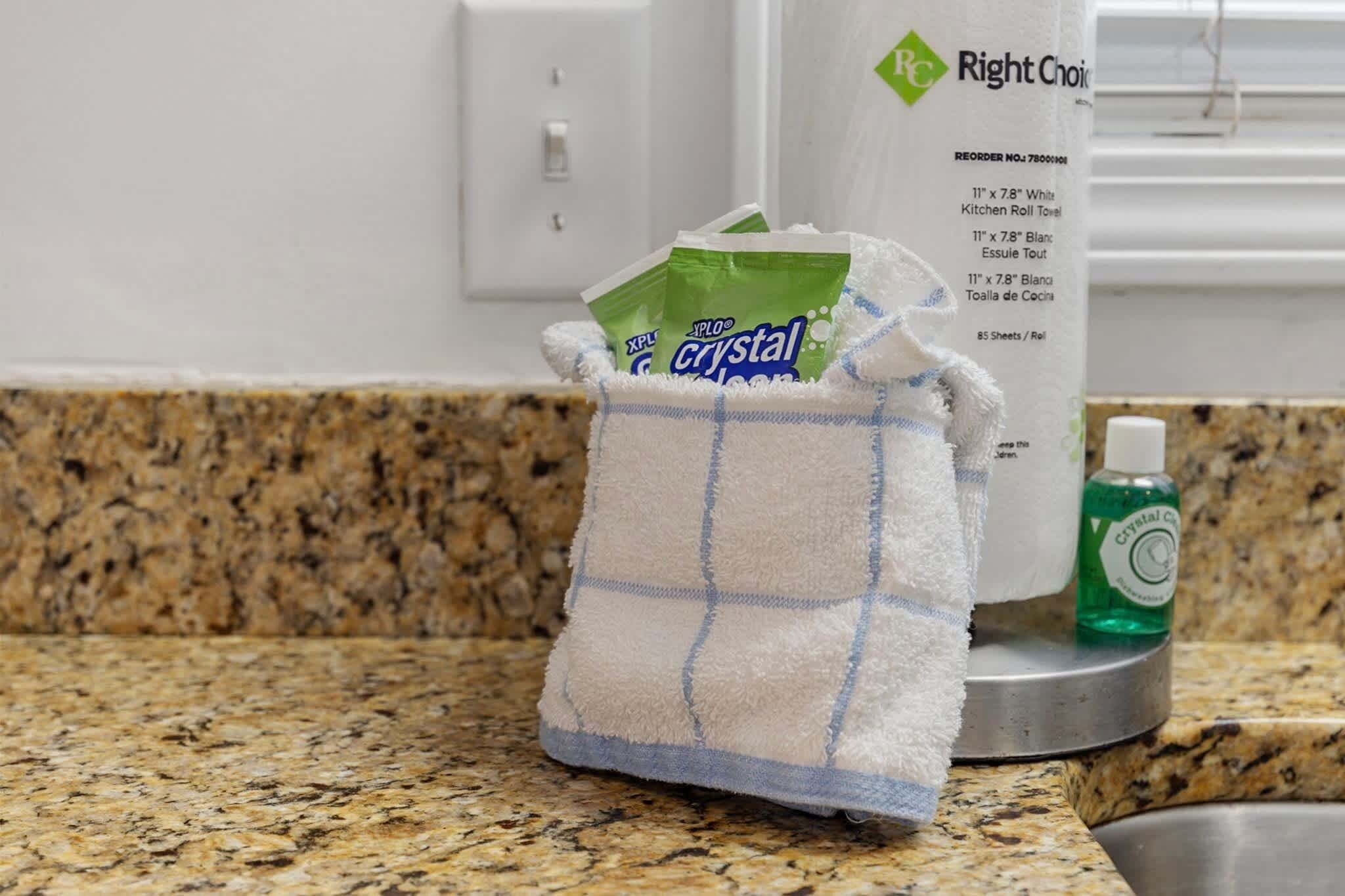 Una encimera de cocina con una toalla, una botella de Crystal Clear detergente para platos y un recipiente blanco con la etiqueta 'Right Choice'.