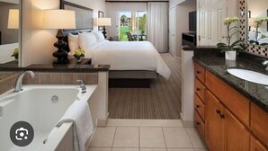 A hotel room with a large bed, a separate bathroom with a bathtub, a vanity with a sink, and a large mirror. - Coachella Perfect! Cozy studio, sleeps 4 in Palm Desert with fitness room, AC.  (Palm Desert)