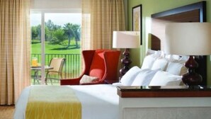 A hotel room with a bed, a red chair, a table with a lamp, and a view of a green landscape through the window. - Coachella Perfect! Cozy studio, sleeps 4 in Palm Desert with fitness room, AC.  (Palm Desert)