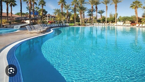 A clear blue pool with lounge chairs and palm trees. - Coachella Perfect! Cozy studio, sleeps 4 in Palm Desert with fitness room, AC.  (Palm Desert)