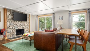 Un salon avec une cheminée en pierre, un téléviseur à écran plat, une table à manger en bois et un tapis vert.