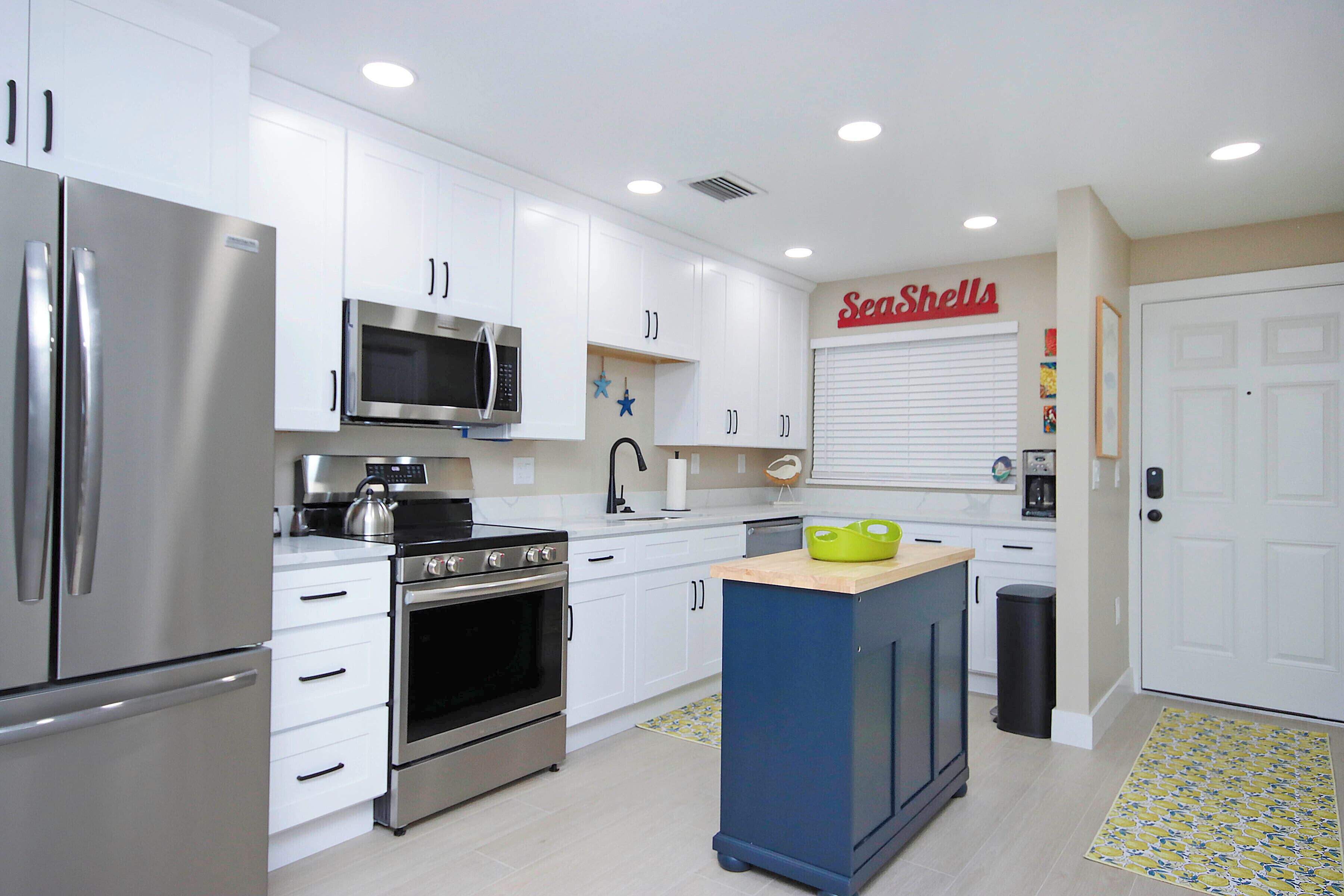 A modern kitchen with stainless steel appliances, white cabinetry, and a blue island.