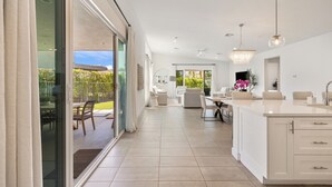 A modern kitchen with a large island, white cabinetry, and a view to the outdoors. - Harlow House - Lounge poolside in Indian Wells (Indian Wells)