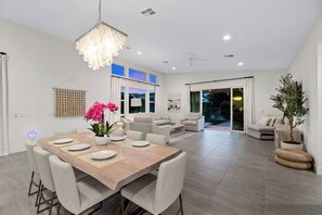 A modern dining area with a wooden table, grey upholstered chairs, and a hanging chandelier. - Harlow House - Lounge poolside in Indian Wells (Indian Wells)