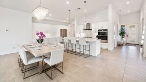 A modern kitchen with white cabinets, a central island, bar stools, and pendant lighting. - Harlow House - Lounge poolside in Indian Wells (Indian Wells)