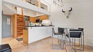 Eine moderne Küche mit Holzausstattung, einem Edelstahlkühlschrank und einer Essecke mit Barhocker.