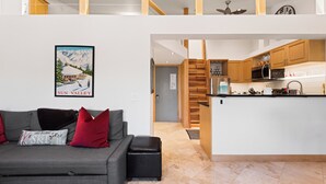 Eine moderne Wohnung mit einem grauen Sofa, roten Kissen, einer Holztreppe und einer Küche mit Holzausziehtüren und einer schwarzen Arbeitsplatte.