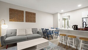 A modern living room with a grey sofa, blue chairs, a coffee bar, and a kitchen area with white cabinets and a stainless steel refrigerator. - Modern Studio in Austin - Fast WiFi + Washer/Dryer (Austin)
