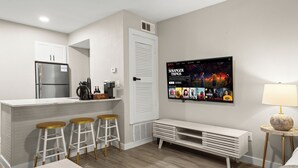 A modern kitchen with a refrigerator, white cabinets, and a bar area with stools. - Modern Studio in Austin - Fast WiFi + Washer/Dryer (Austin)