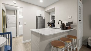 A modern kitchen with a central island, bar stools, a refrigerator, and a coffee machine. - Modern Studio in Austin - Fast WiFi + Washer/Dryer (Austin)