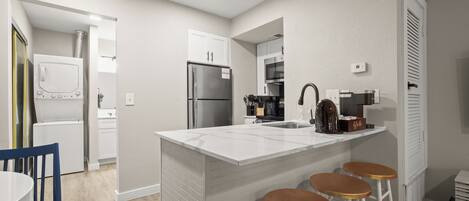 A modern kitchen with a central island, bar stools, a refrigerator, and a coffee machine.
