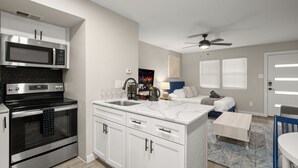 A modern kitchen with a built-in microwave, oven, and sink. There is a dining area with a table and chairs, and a ceiling fan above. - Modern Studio in Austin - Fast WiFi + Washer/Dryer (Austin)