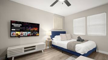 A modern bedroom with a bed, a TV mounted on the wall, a ceiling fan, and a window with blinds.