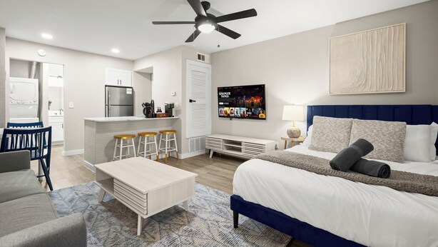 A modern hotel room with a bed, a desk, a kitchenette, and a TV. - Modern Studio in Austin - Fast WiFi + Washer/Dryer (Austin)