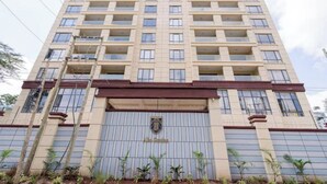 A tall, beige multi-story building with a central entrance and a logo above the door.