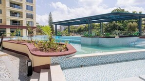 A swimming pool with a tiled edge, surrounded by a covered area and a building in the background.