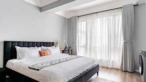 A modern bedroom with a large bed, a headboard, a nightstand, and a window with curtains.