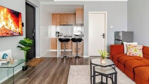 A modern living room with a glass coffee table, a sofa, and a TV displaying a fireplace.
