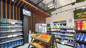 A grocery store interior with shelves stocked with bottled water, a fruit display, and various household products.
