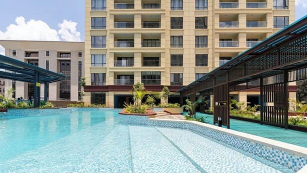 A swimming pool with a tiled edge, surrounded by a building with multiple balconies and a covered walkway.