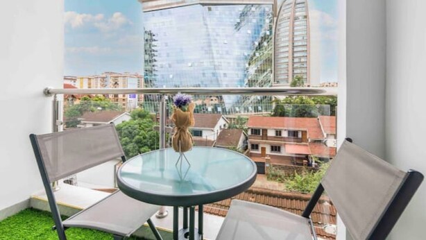 A balcony with a glass table and two chairs, overlooking a cityscape with modern buildings.