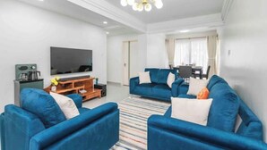 A modern living room with a blue sofa set, a flat-screen TV, and a wooden entertainment unit.