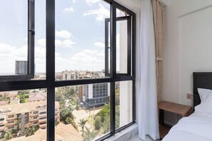 Ein Hotelzimmer mit großem Fenster und Blick auf die Stadt sowie umliegende Gebäude.