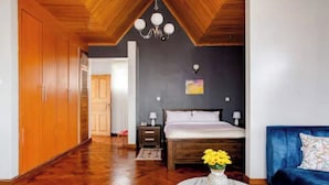 A bedroom with a wooden ceiling, a bed with white bedding, a nightstand, a blue sofa, and a vase with flowers on a round table.