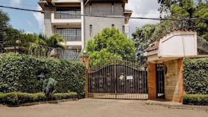 A gated residential property with a two-story building, a paved driveway, and a well-maintained hedge.
