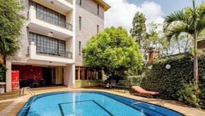A swimming pool with a clear blue water feature, surrounded by a building with balconies and a lush green hedge.