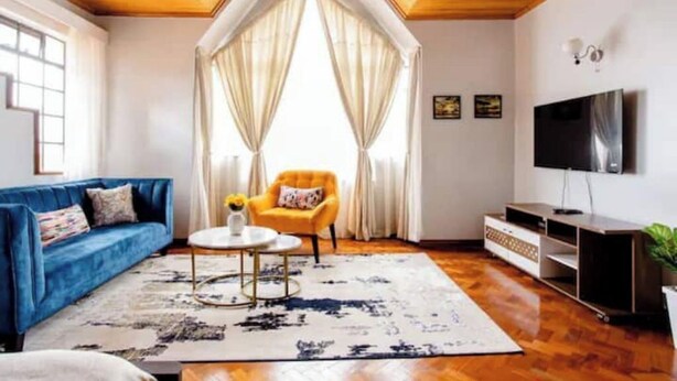 A living room with a blue sofa, a yellow armchair, a TV, and wooden flooring.