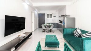 Ein modernes Wohnzimmer mit Flachbildfernseher, einem grünen Sofa und einem Essbereich mit Tisch und Stühlen.