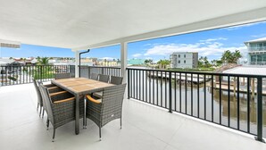 Un balcon avec une table et des chaises, une balustrade et une vue sur une étendue d’eau et des bâtiments.