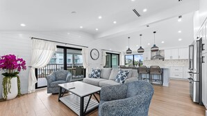 Un salon moderne avec un canapé, une table basse et des fauteuils, une cuisine équipée d’appareils  électroménagers en acier inoxydable et un balcon avec vue.