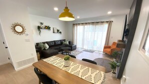 Uma sala de estar moderna com sofá, mesa de jantar com cadeiras e uma janela grande com cortinas.