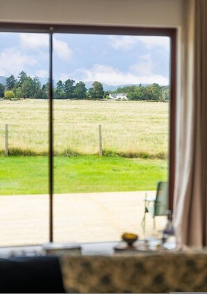 Een kamer met een groot raam met uitzicht op een grasveld en bomen.