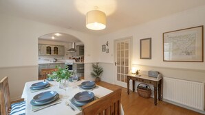 Un coin repas avec une table dressée pour quatre personnes, une cuisine en arrière-plan et une carte accrochée au mur.